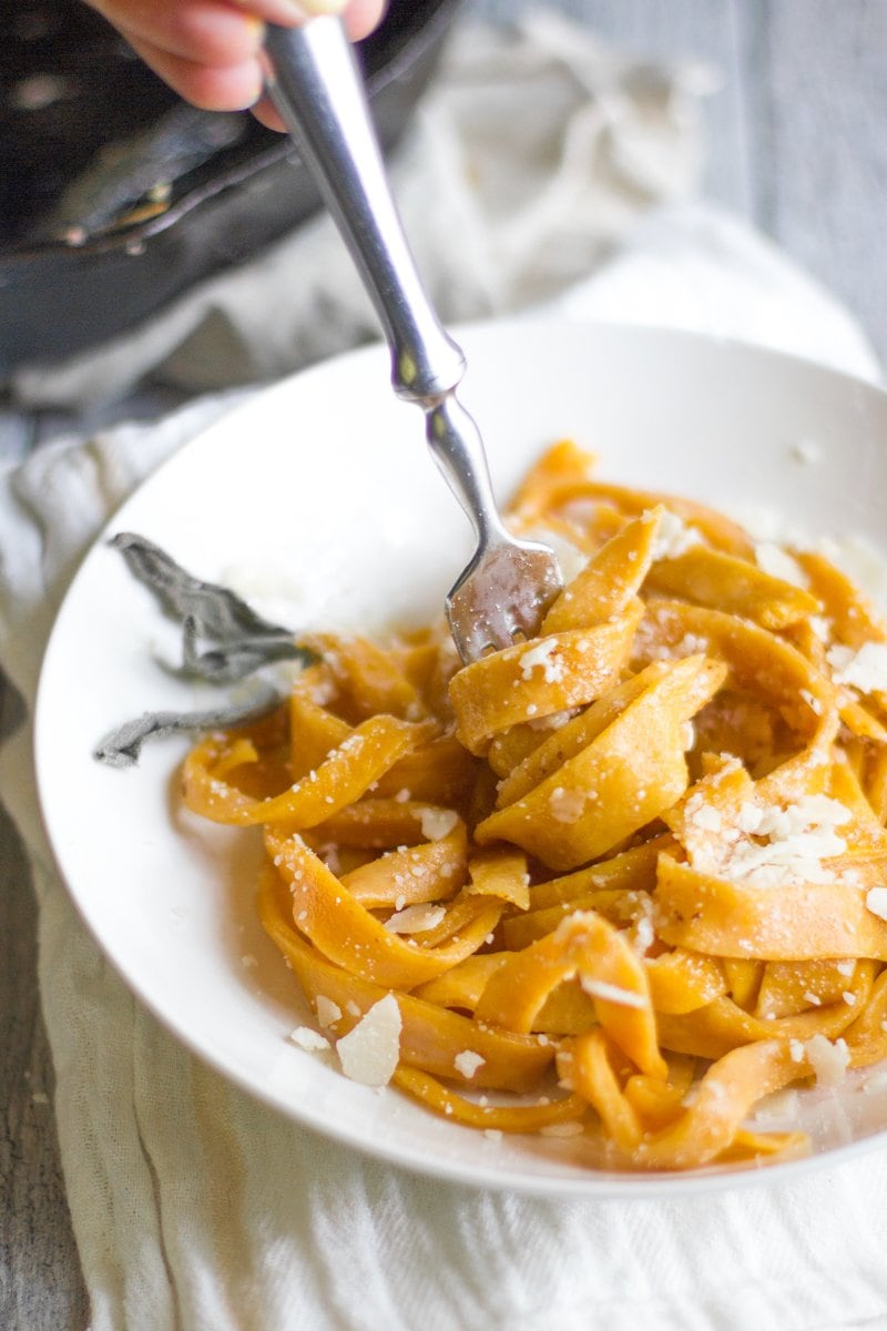 A fork twirls fresh pumpkin pasta on a white plate.