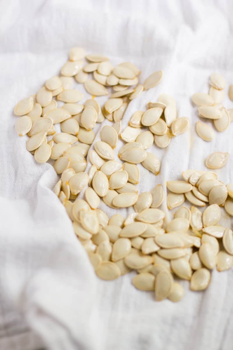 Clean, raw pumpkin seeds are on a white kitchen towel to get dried off.