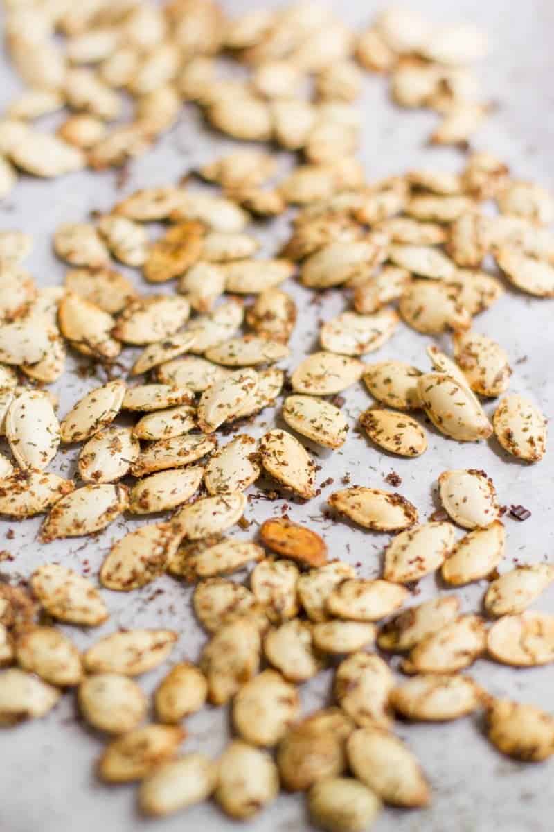 Close up view of roasted pumpkin seeds with seasoning on a parchment-paper lined baking sheet.