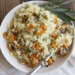 A bowl of butternut squash rice garnished with fresh sage leaves on a tabletop