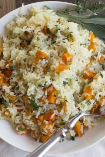 A bowl of butternut squash rice garnished with fresh sage leaves on a tabletop