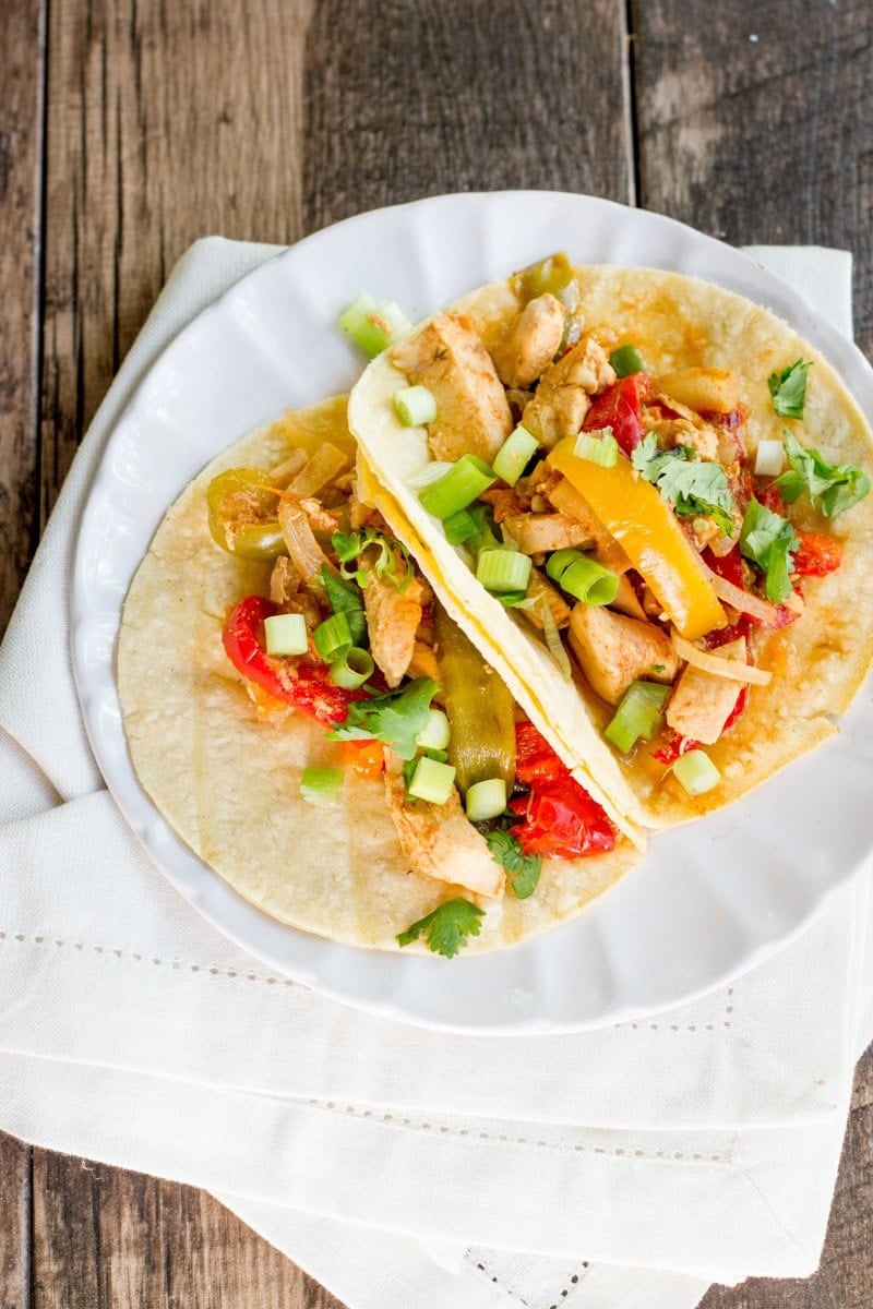 Two Slow Cooker Chicken Fajitas sit next to each other on a plate.