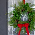 Evergreen wreath hanging from a red ribbon on a front door.