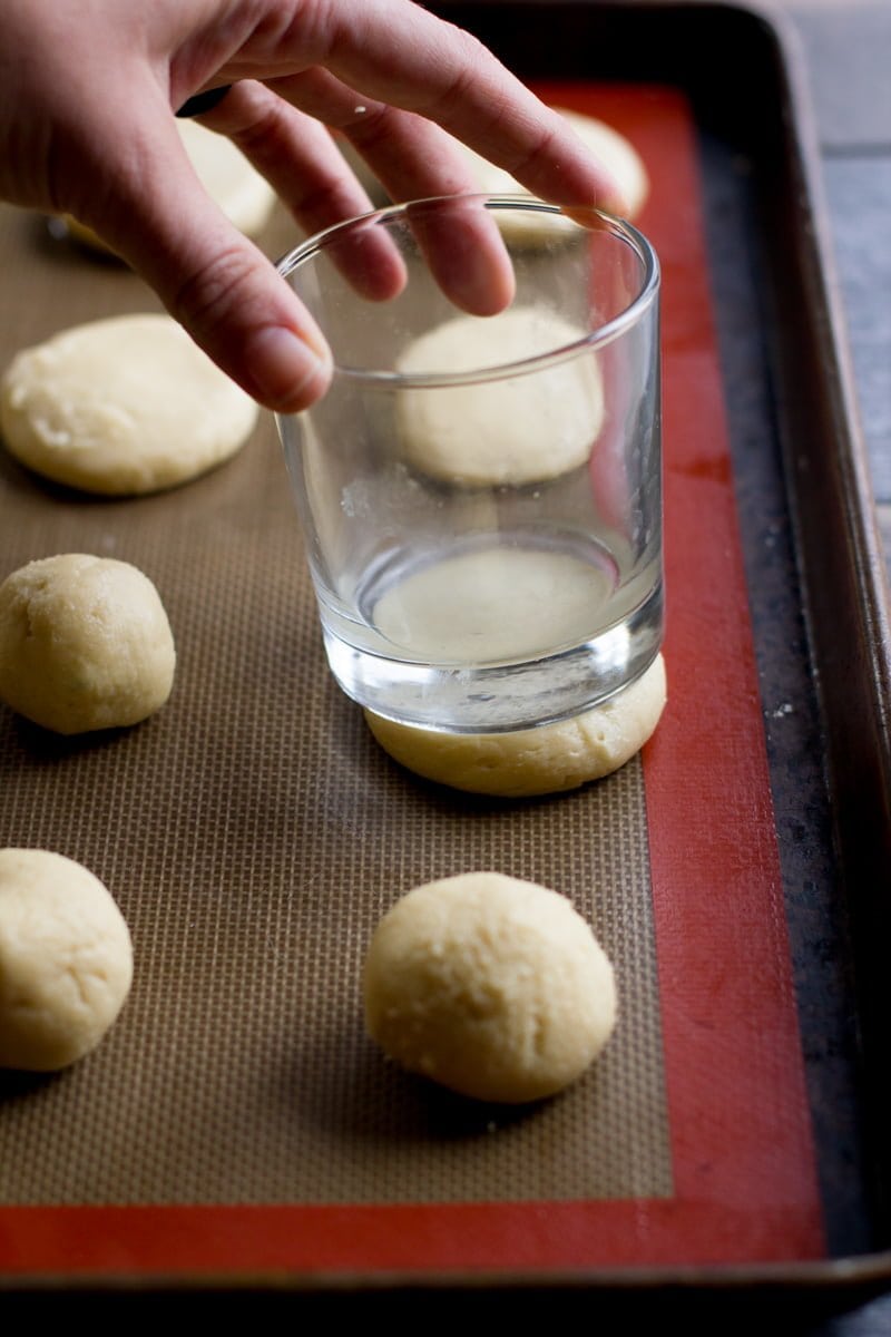 Balls of dough for Lofthouse Sugar Cookies being pressed down with an empty glass