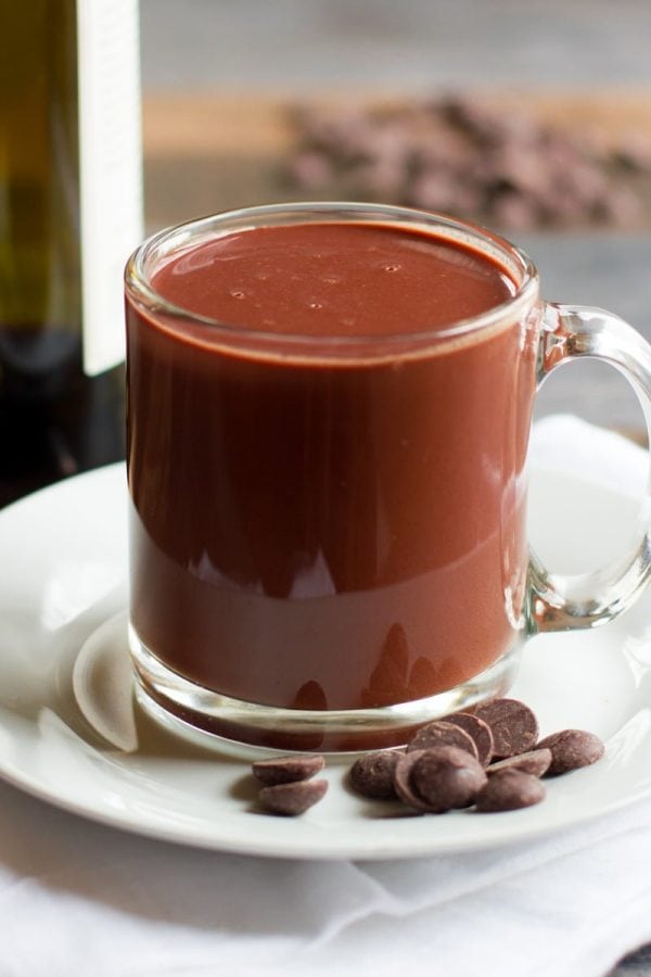 Clear glass mug of Red Wine Hot Chocolate on a white saucer with chocolate chips