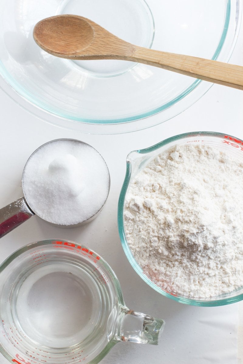 The ingredients for the salt dough recipe—flour, salt, and water—lie flay on a white countertop.