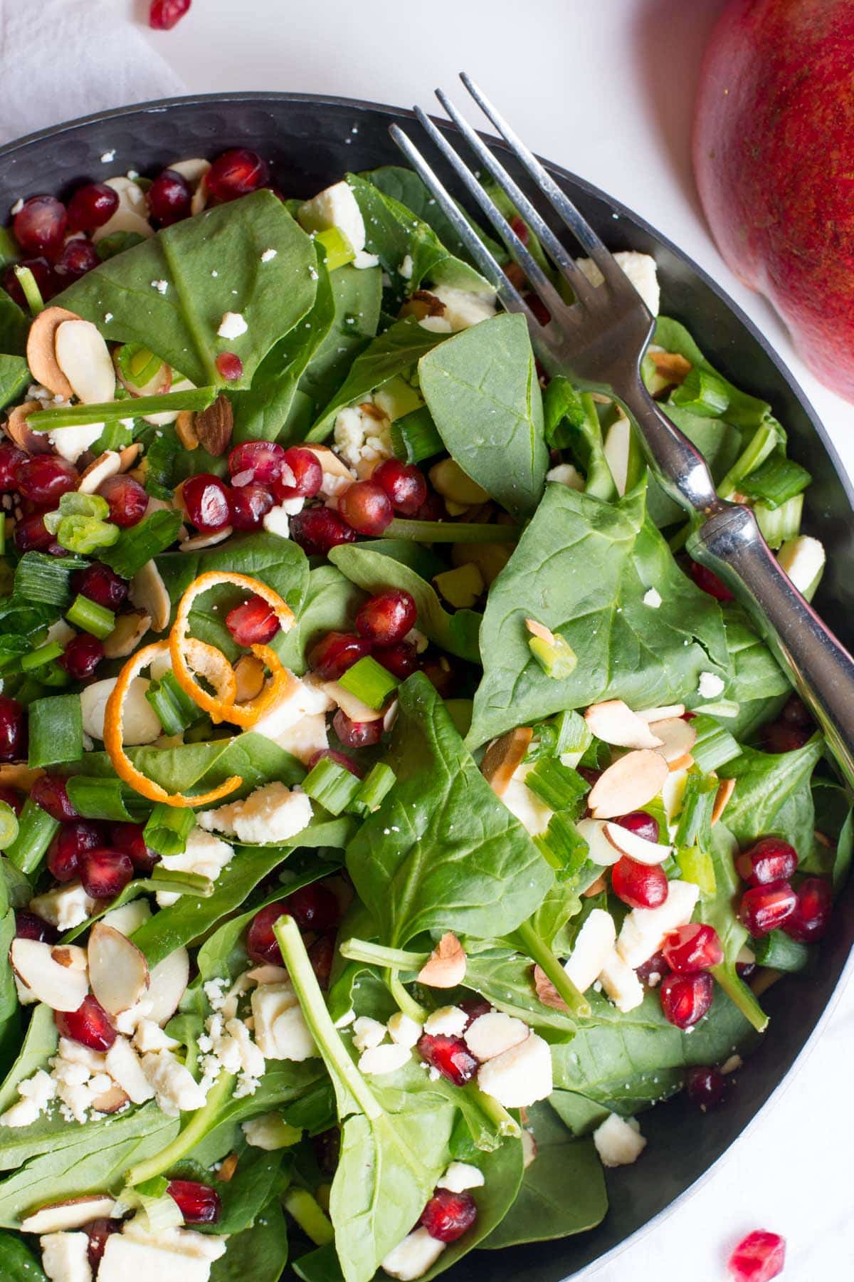 Close view of spinach and pomegranate salad in a shallow bowl with a fork.