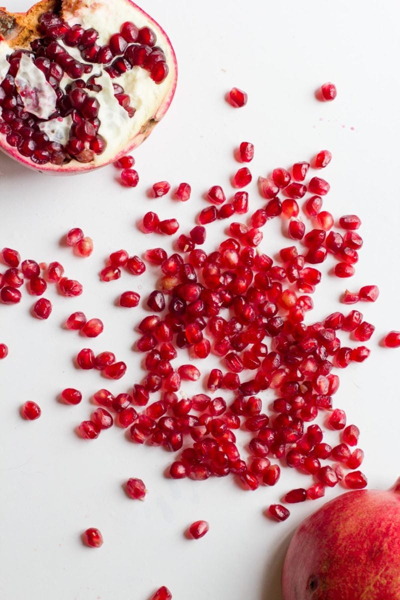 Overhead of two pomegranate halves with pomegranate arils across a white countertop.