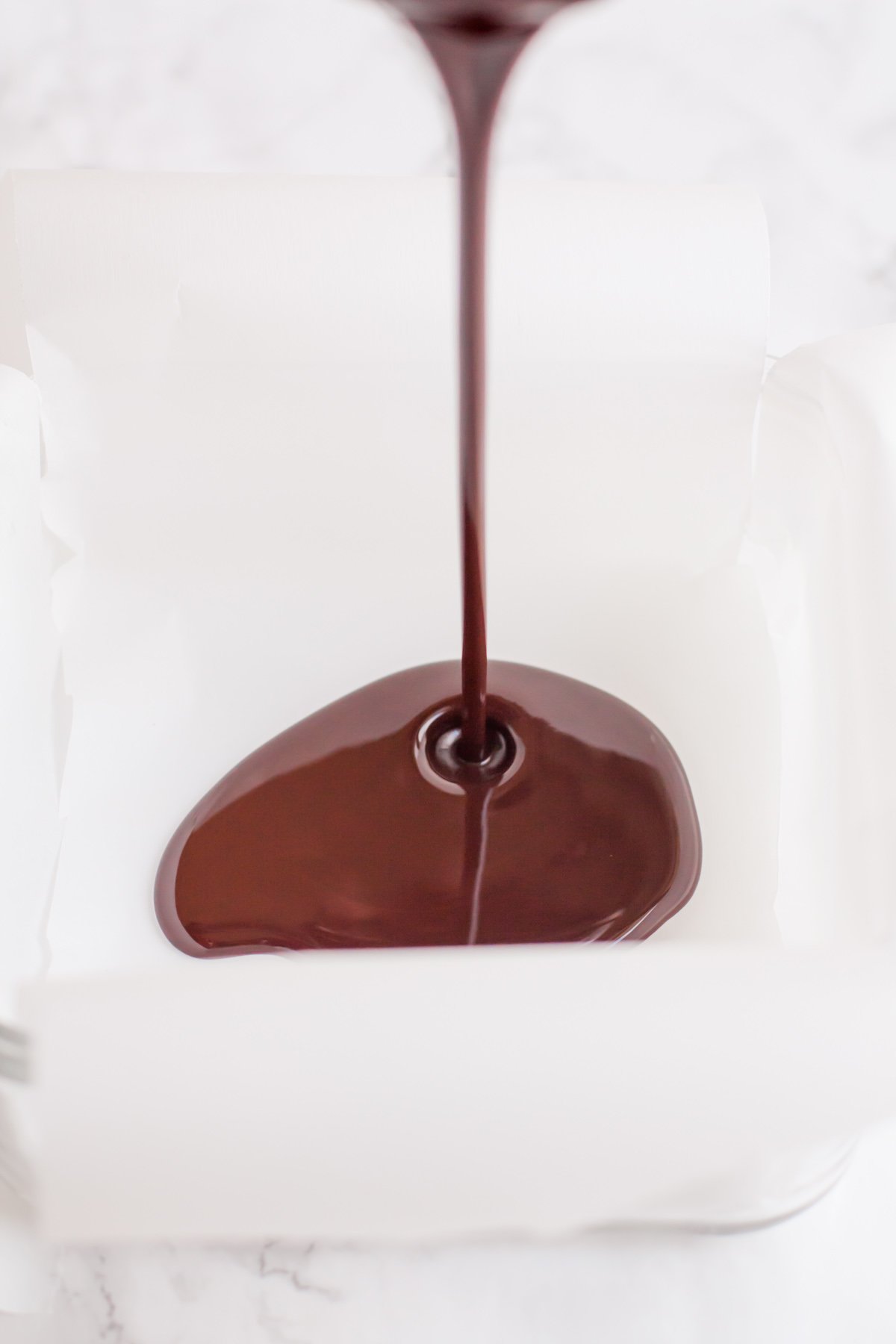 Melted coconut oil and cocoa powder being poured into a parchment paper-lined pan.