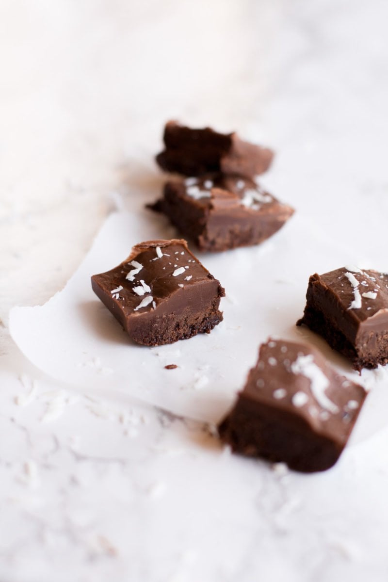 Squares of vegan fudge sprinkled with coconut on parchment paper.
