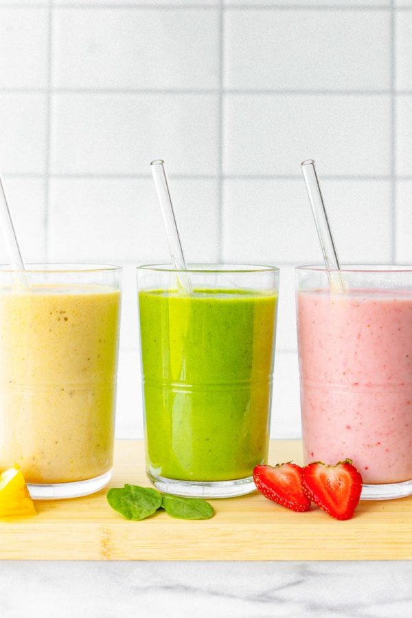 Three colorful fruit smoothies are lined up, each with a glass straw sticking out of it.