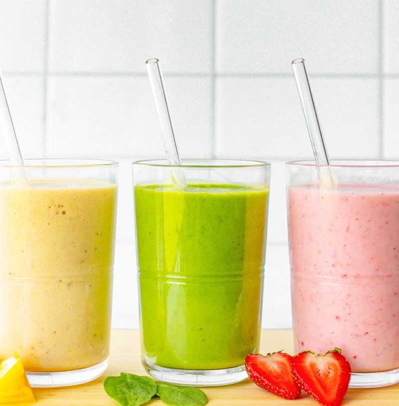 Three colorful fruit smoothies are lined up, each with a glass straw sticking out of it.