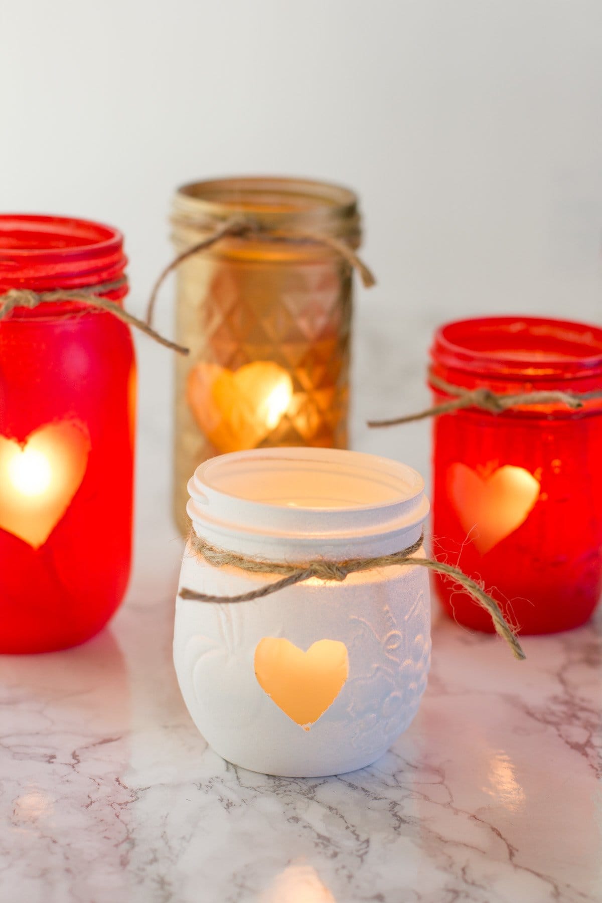 Cluster of Painted Mason Jar Votive Holders, each with a heart and a piece of twine. The jars are gold, red, and white.