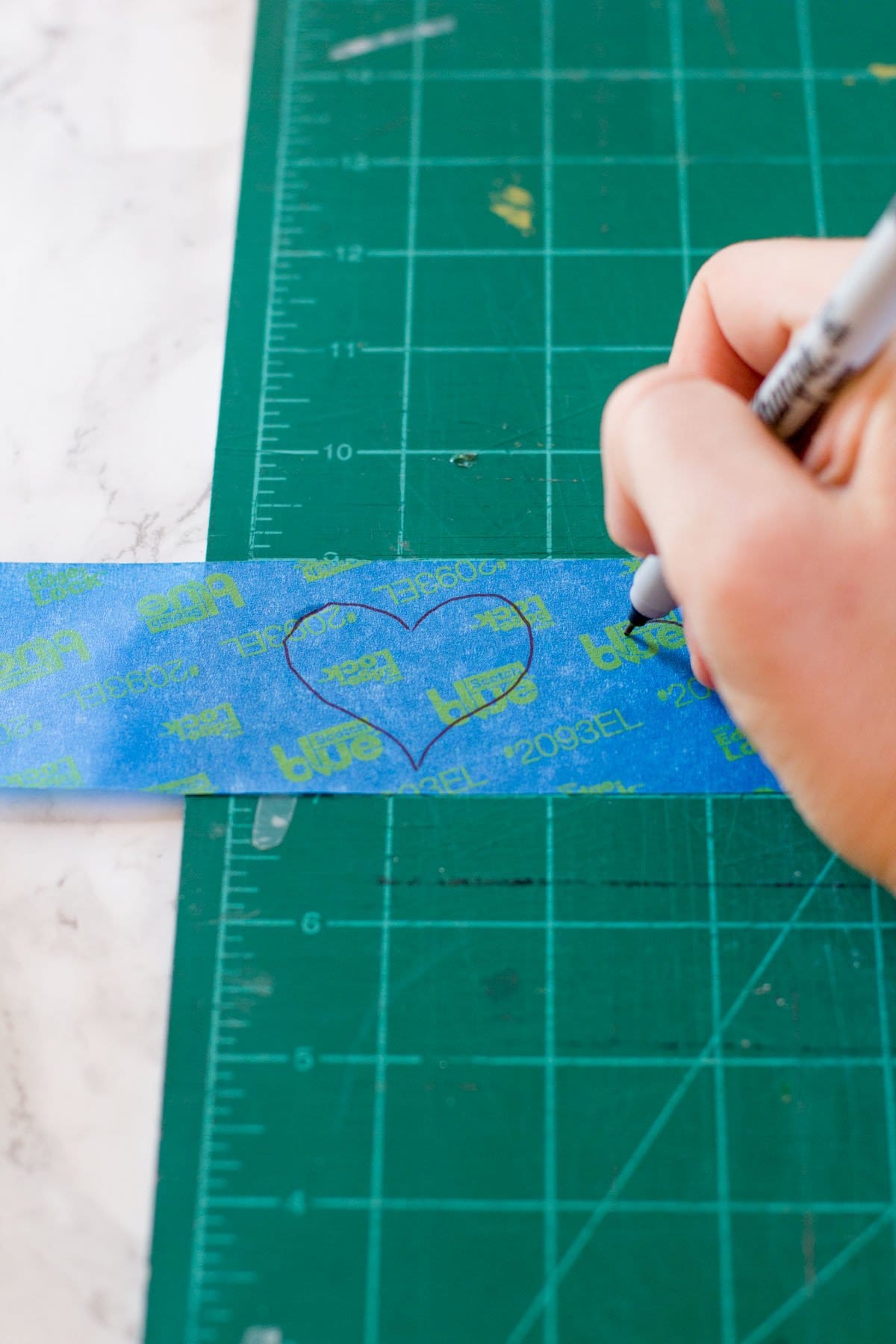 Hand using a Sharpie to draw hearts on a piece of painter's tape
