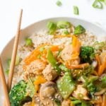 Overhead shot of Healthy Chicken Stir Fry on top of brown rice in a white bowl with crossed chopsticks. A text overlay reads "Healthy Chicken Stir Fry."