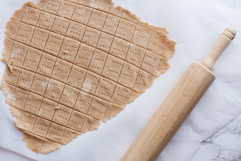 A rolling pin sits near formed cracker dough.