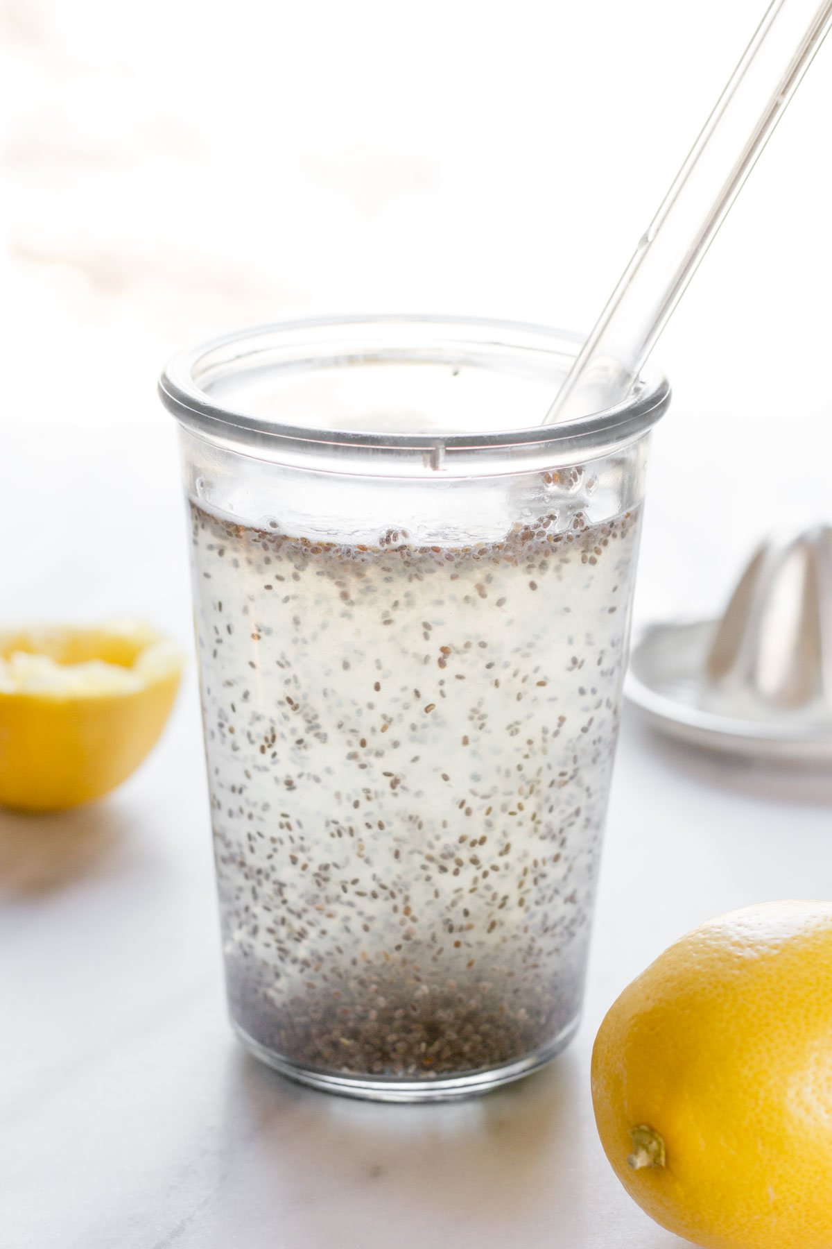 Close-up of glass filled with chia seed drink and glass straw and fresh lemons.