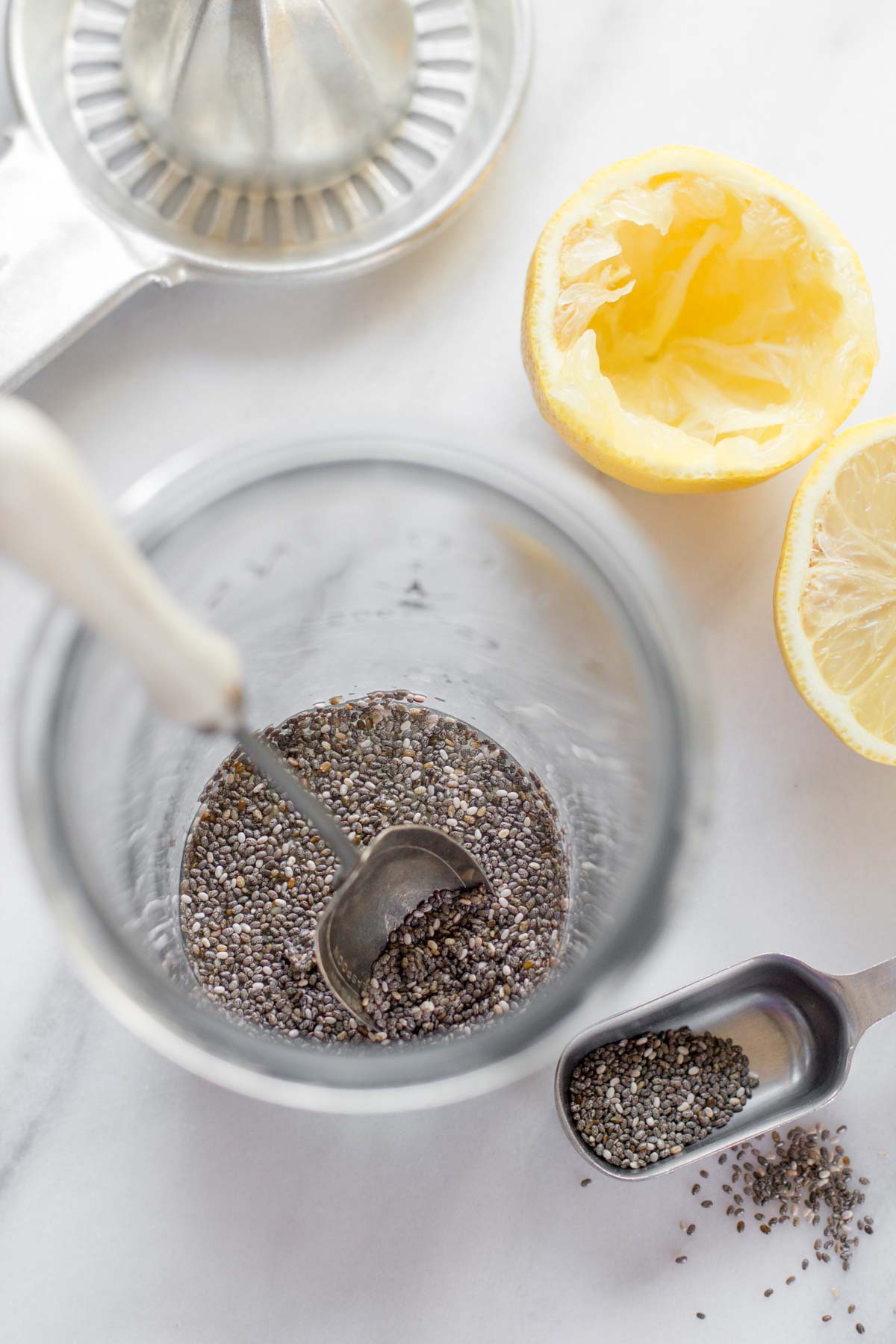 Overhead of chia seeds and a measuring spoon in a tall glass with fresh juices lemon halves.