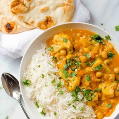 Cauliflower and Chickpea Curry in a white bowl with rice, with a spoon nearby