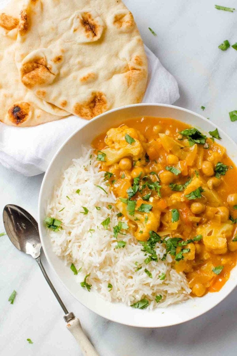 Cauliflower and Chickpea Curry in a white bowl with rice, with a spoon nearby