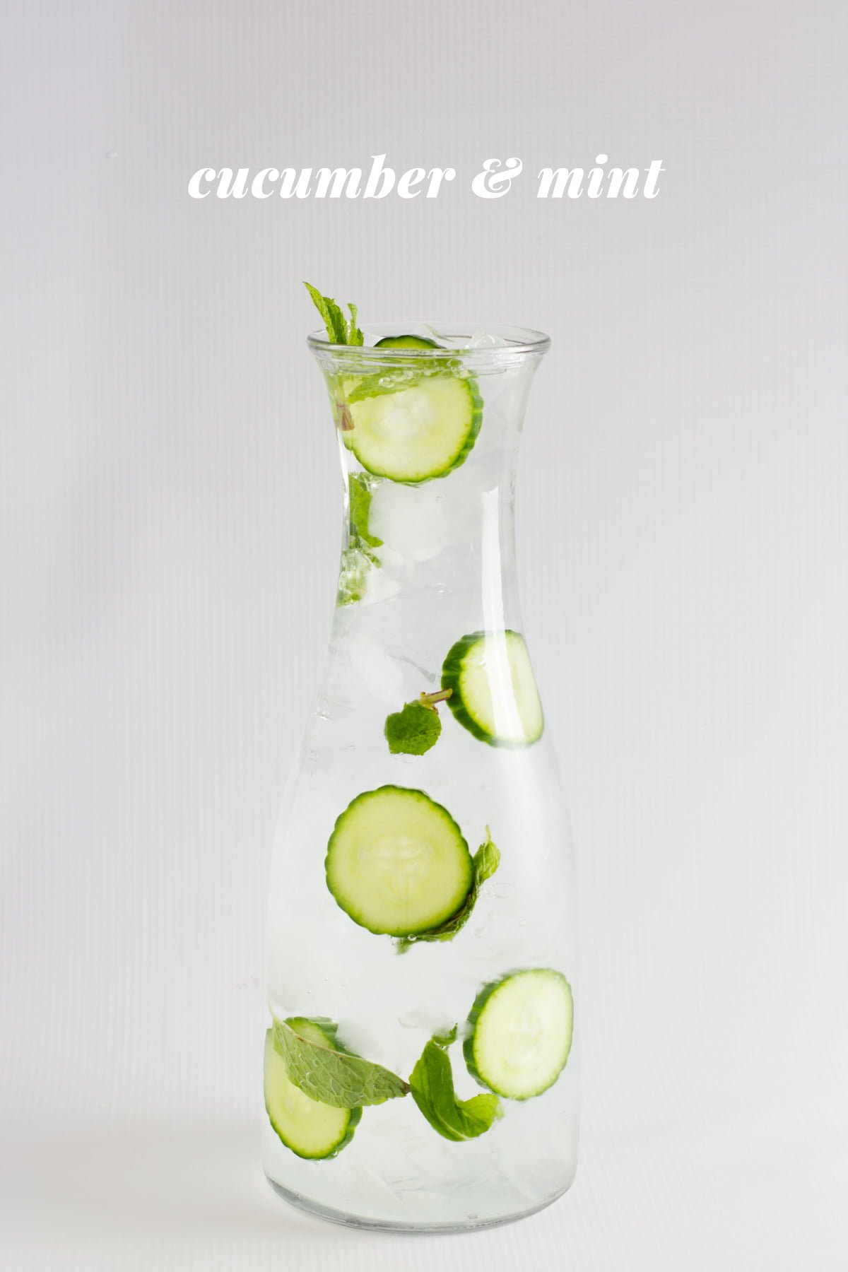 Cucumber and mint infused water is displayed in a glass carafe. A text overlay reads, "Cucumber & Mint."