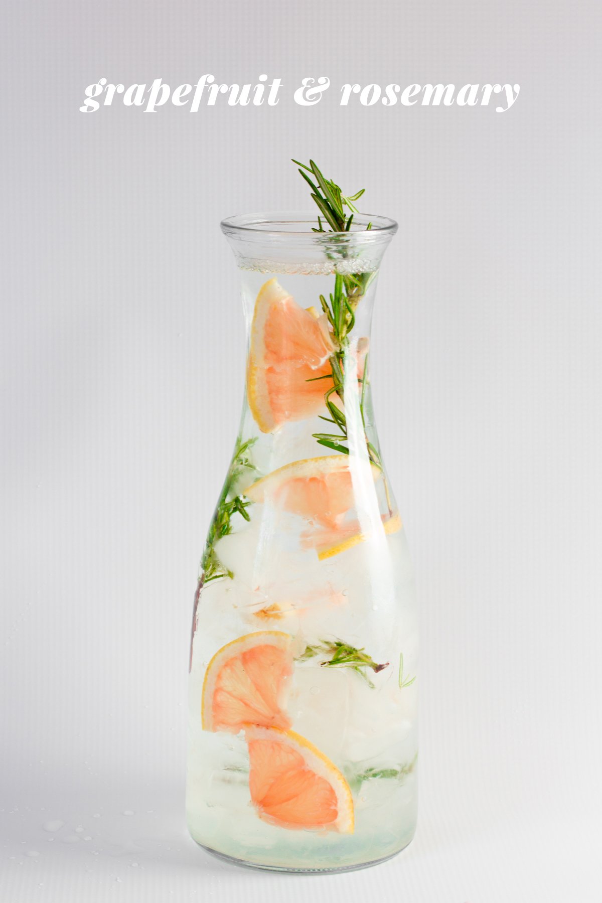 Grapefruit and rosemary infused water is displayed in a glass carafe. A text overlay reads, "Grapefruit & Rosemary."