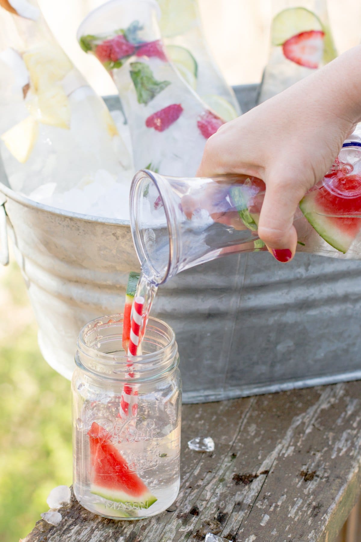 Close-up of pouring watermelon infused water from a glass carafe into a mason jar.