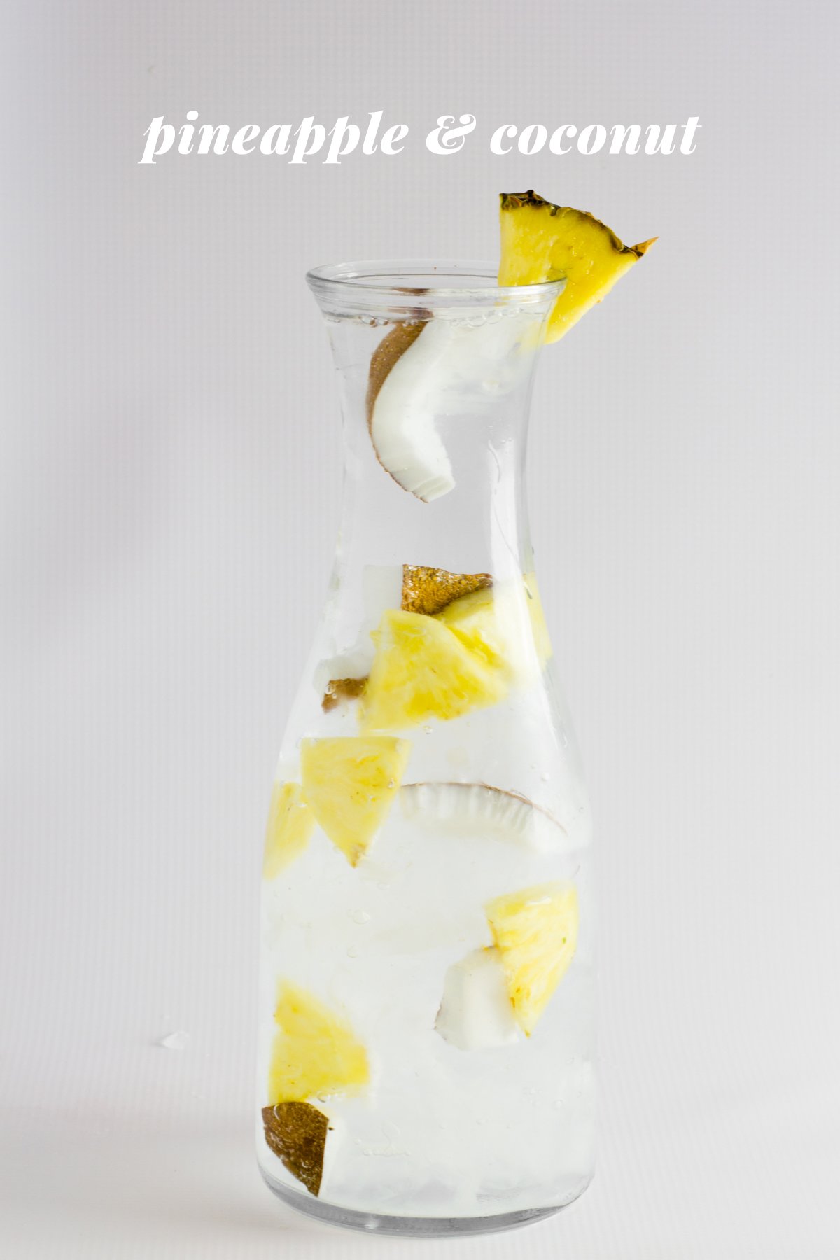 Pineapple and coconut infused water is displayed in a glass carafe. A text overlay reads, "Pineapple & Coconut."
