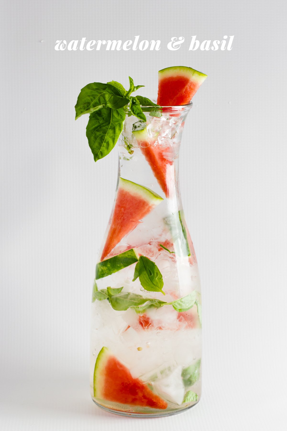 Watermelon and basil infused water is displayed in a glass carafe. A text overlay reads, "Watermelon & Basil."
