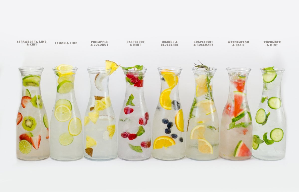 Eight glass carafes of infused water are lined up side-by-side with text above detailing the flavors inside.