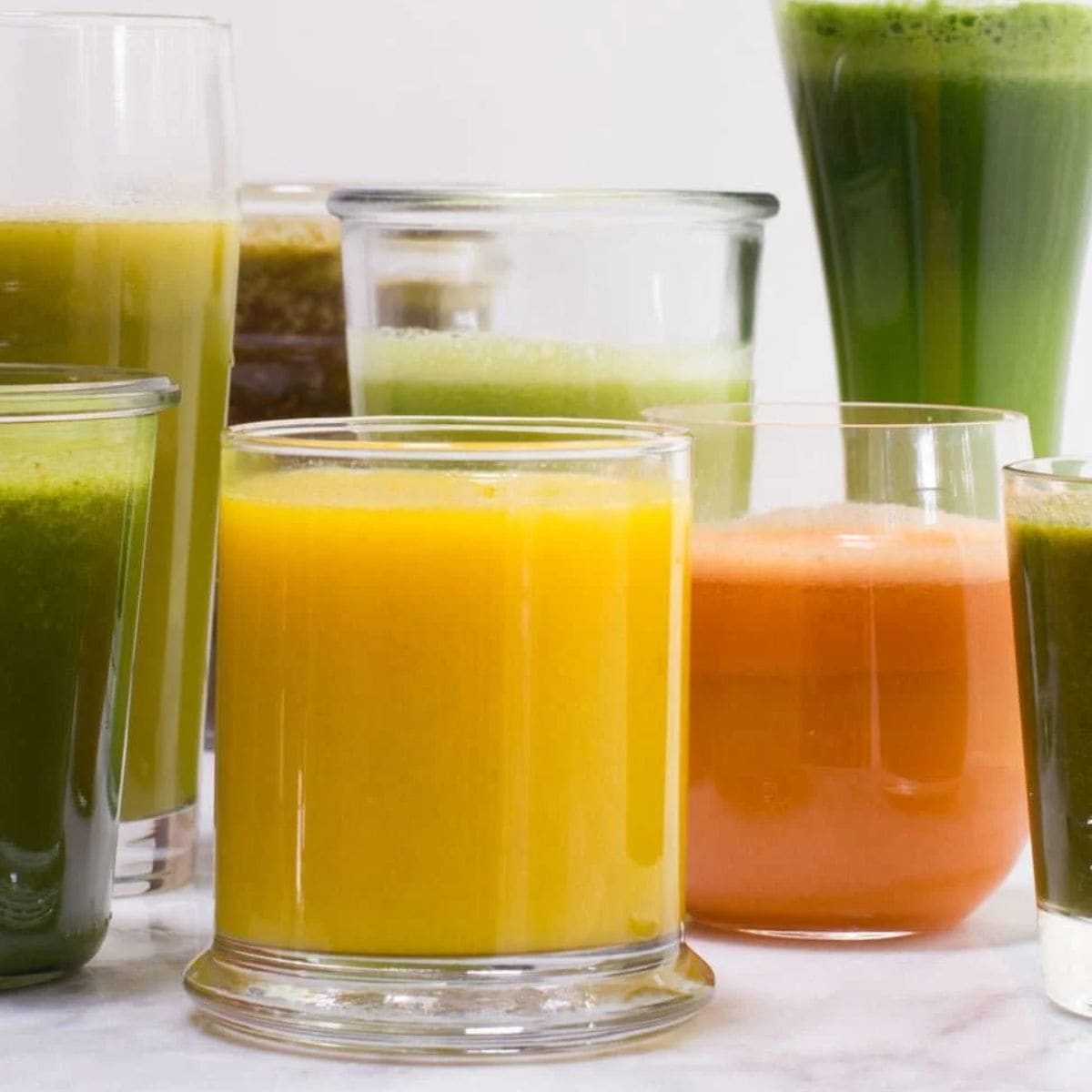 Several glasses filled with various green, orange, and yellow fruit and vegetable juice recipes.
