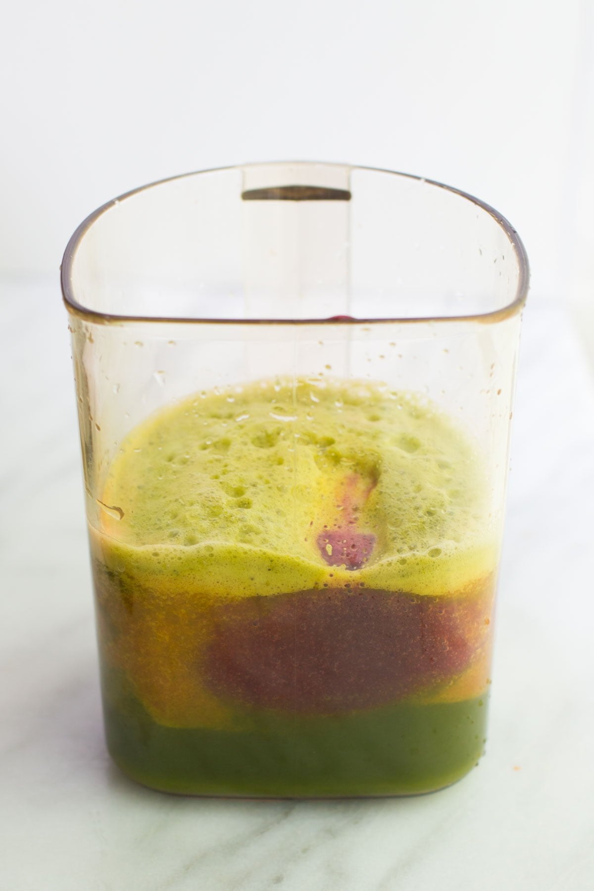 A clear pitcher filled with layered green and red juice recipes, topped with foam.