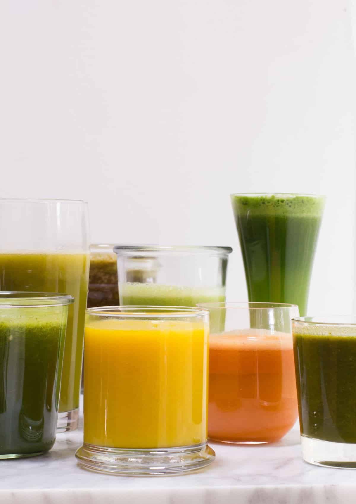 Glasses of varying heights filled with fruit and vegetable juices.