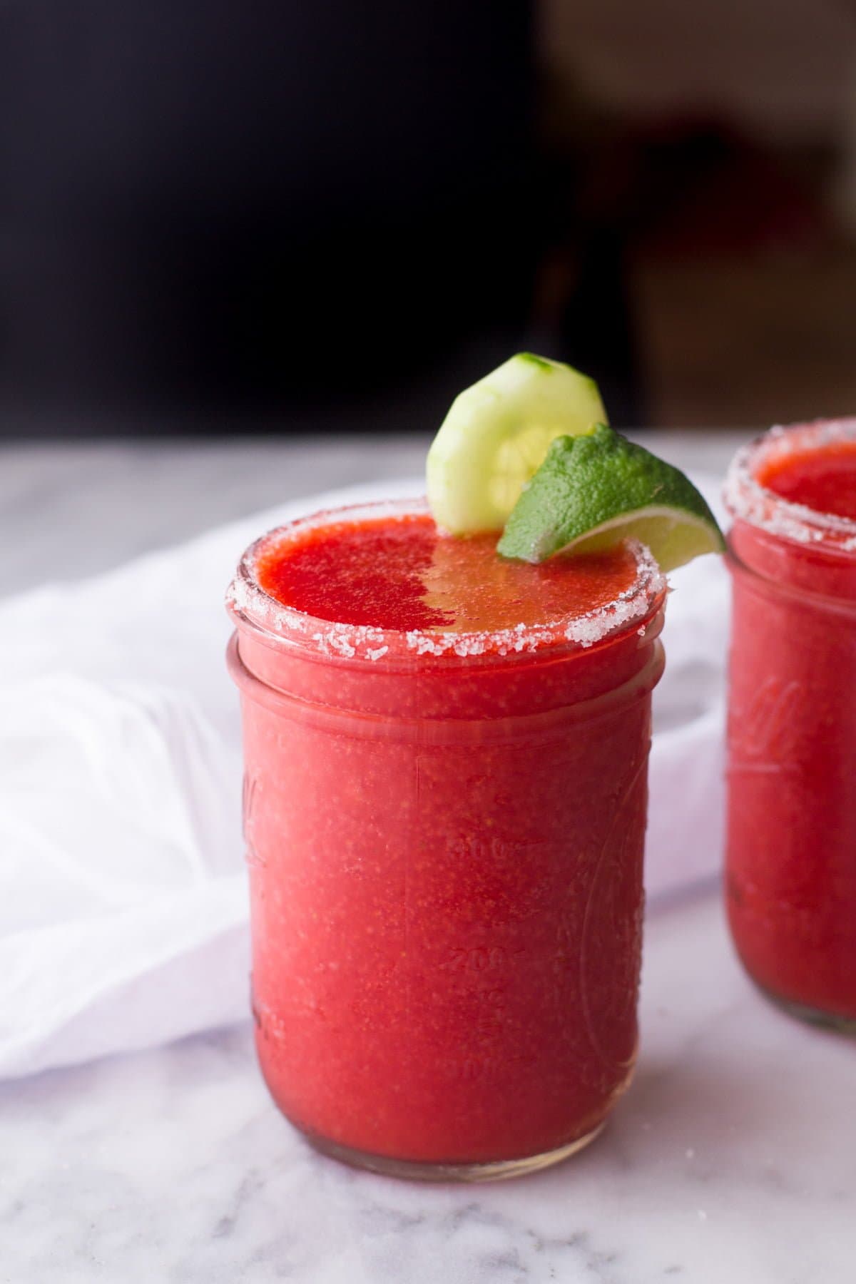 A canning jar used as a drinking glass is rimmed with salt and filled with frozen strawberry cucumber margarita.