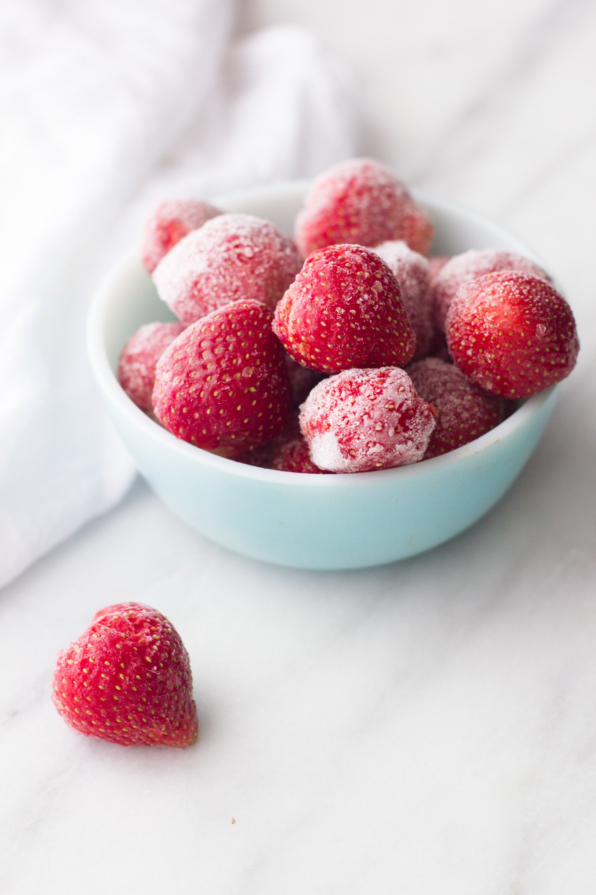 Frozen strawberries piled high in a a bowl with one berry on the counter in front.