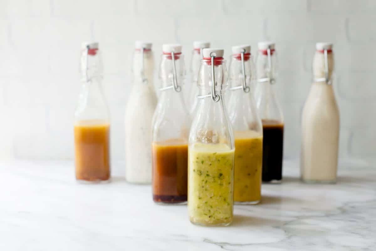 Eight different salad dressings in swing-top bottles on a marble countertop