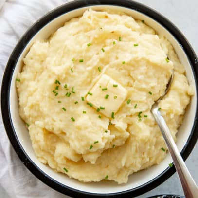 Overhead view of a black and white bowl full of fluffy mashed potatoes with a butter pat melting on top.