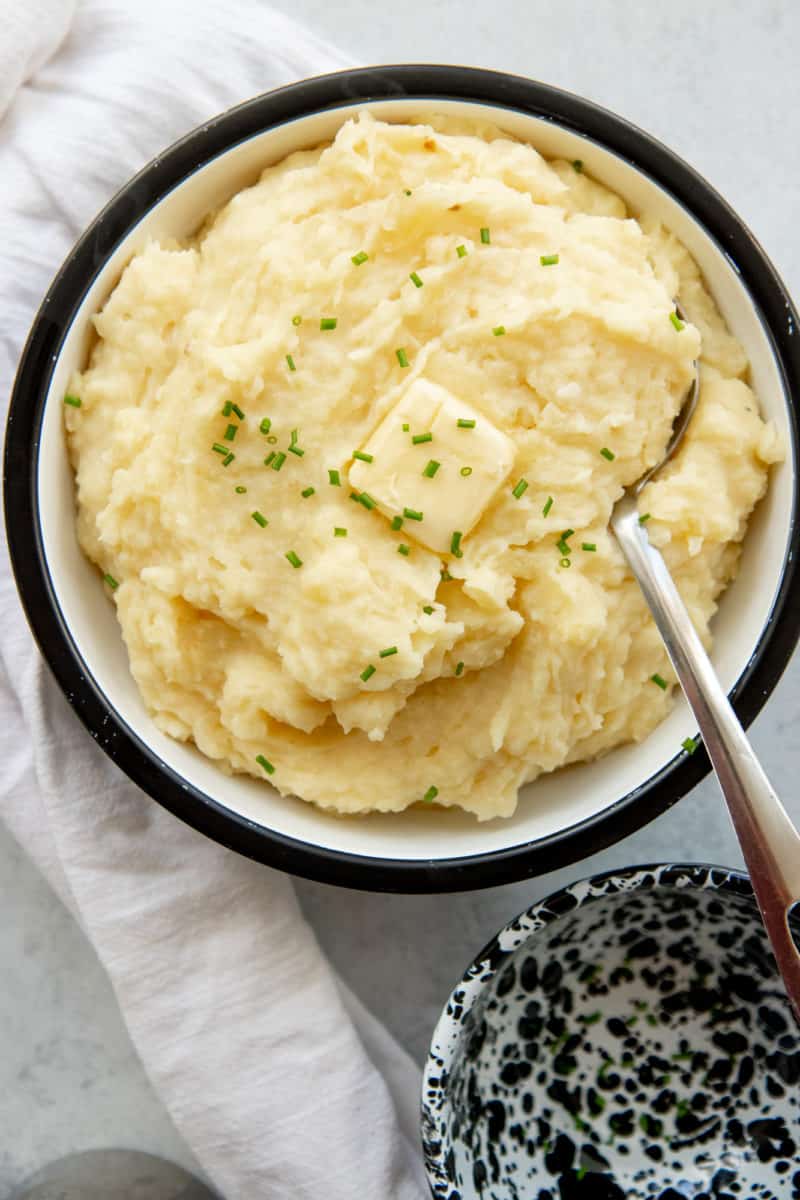 Overhead view of a black and white bowl full of fluffy mashed potatoes with a butter pat melting on top.