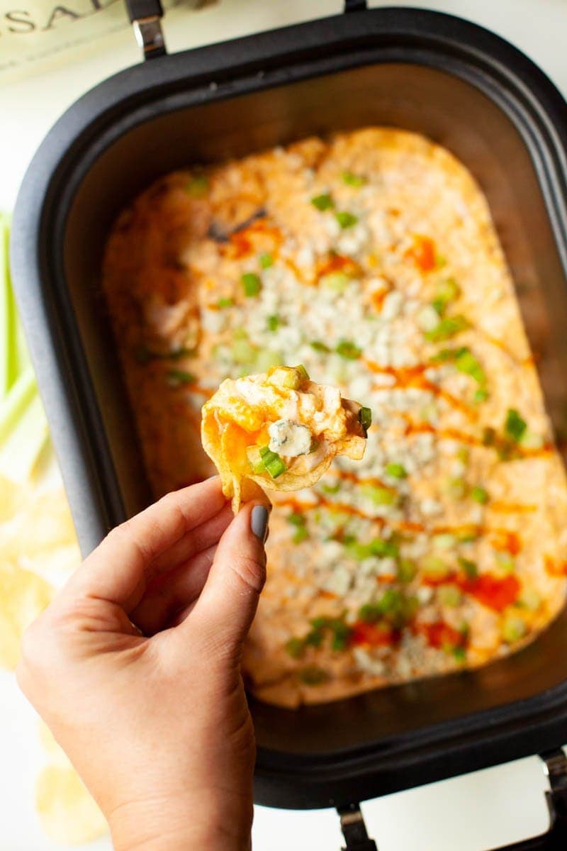 A hand hold up a chip loaded with crackpot buffalo chicken dip.