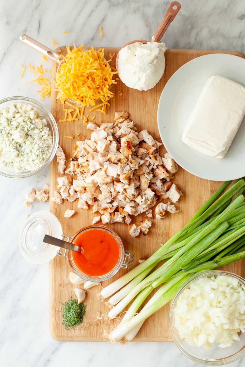 Ingredients for buffalo chicken dip spread out on a wooden cutting board