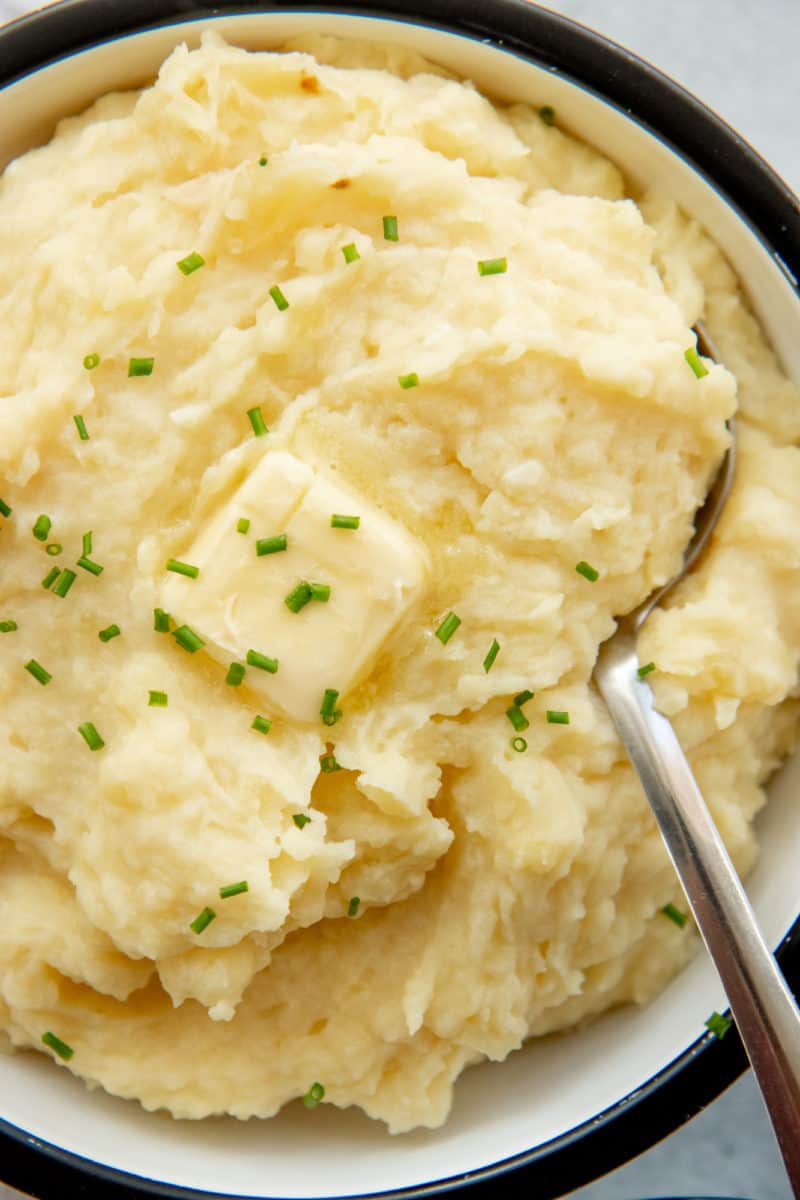 Tight view of creamy mashed potatoes in a bowl with a butter pat melting on top.