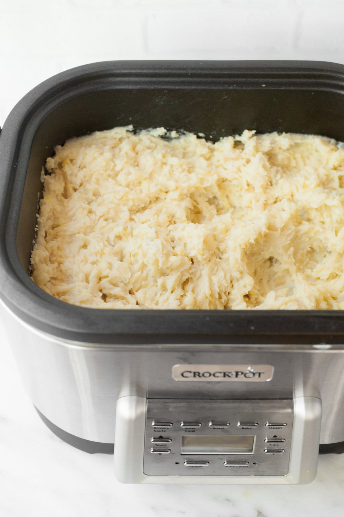 Fluffy mashed potatoes in a large Crock-Pot slow cooker on a white countertop.