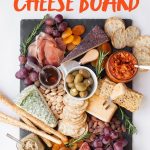 Slate board covered with Cheese, crackers, dried fruit, olives, and sausage. A text overlay reads "How to Make an Awesome Cheese Board"