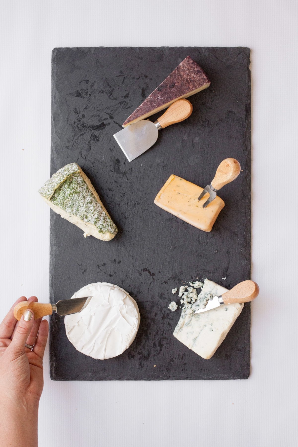 Slate cutting board with 5 wedges of cheese, each with a cheese knife.