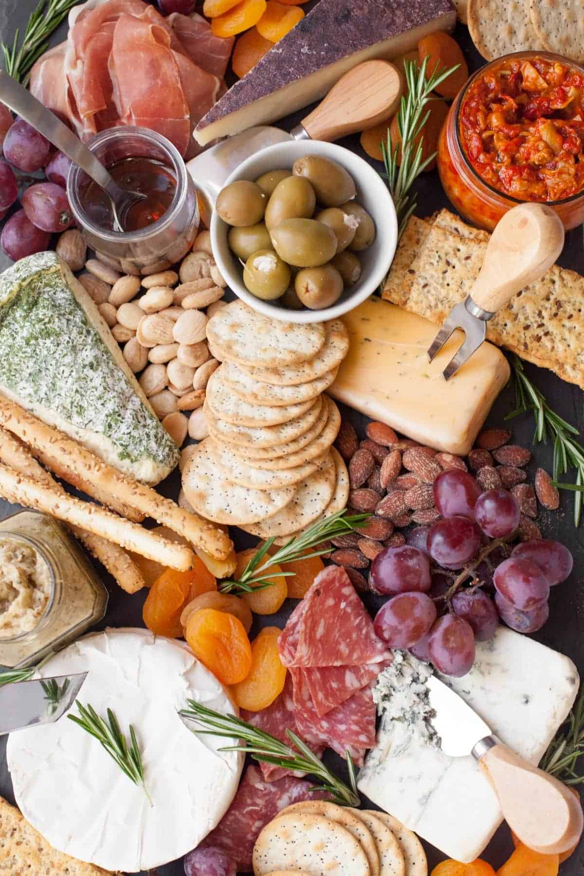 Close up of a cheese board with cheeses, crackers, olives, fruits, and almonds.