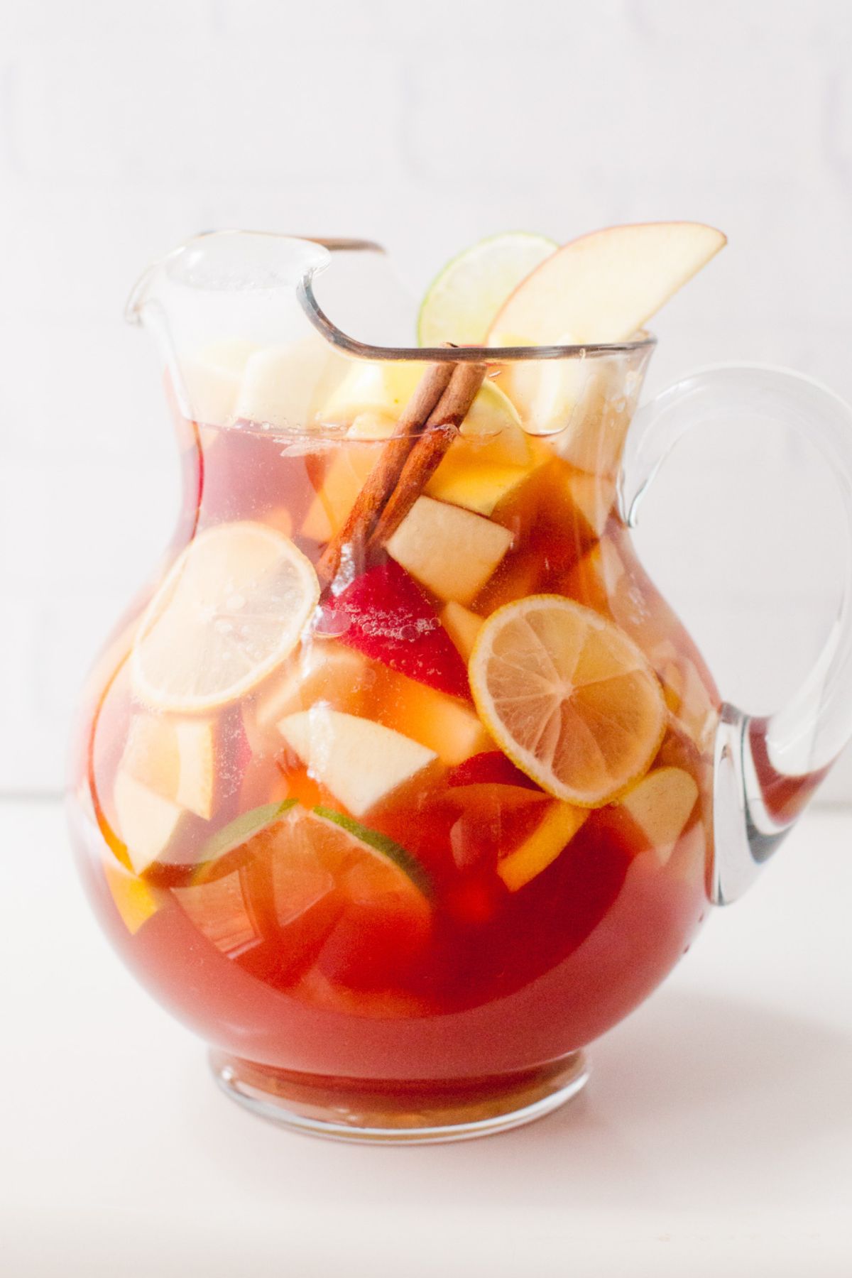 A clear glass pitcher full of rose sangria sits on a white countertop.