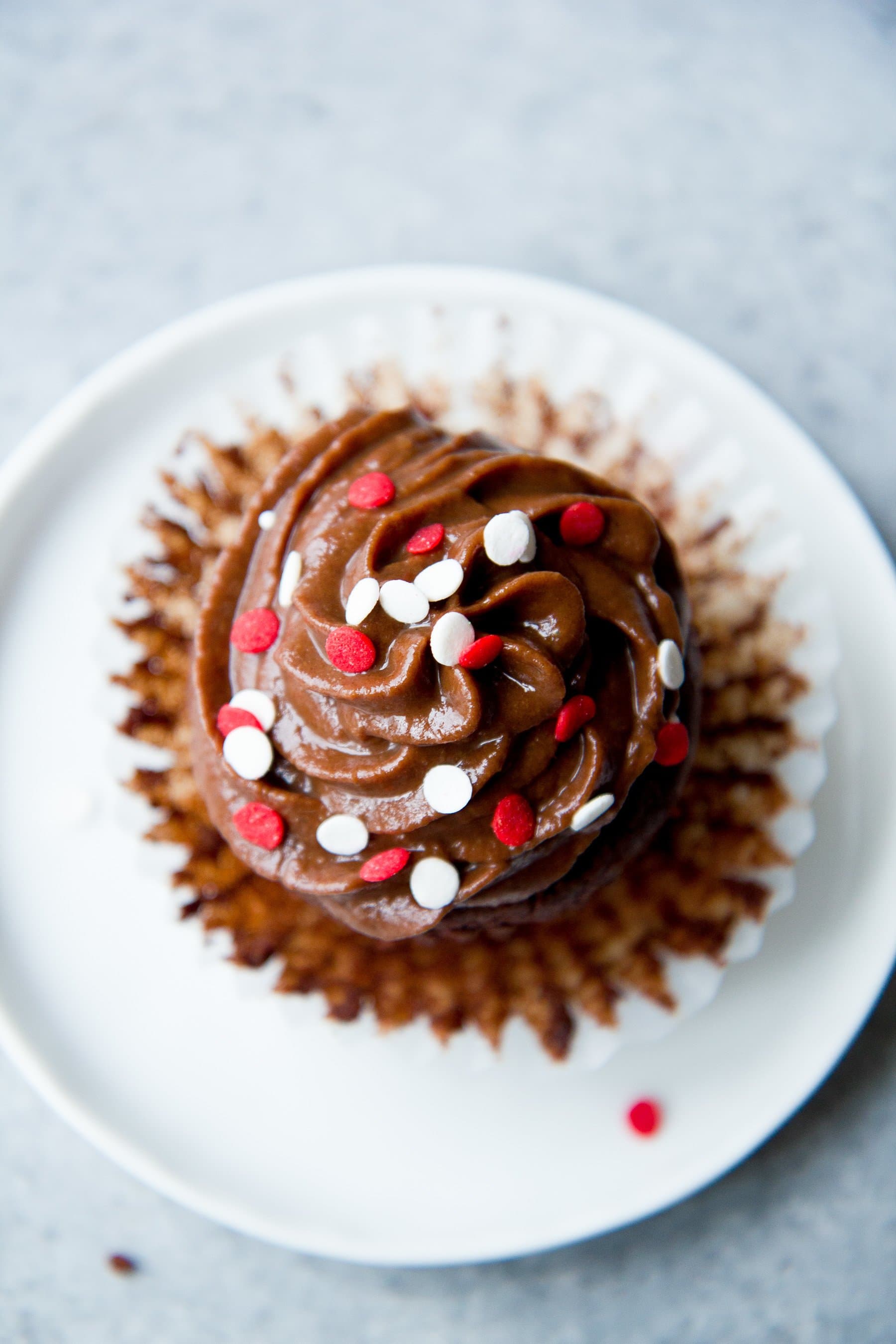 An unwrapped healthier chocolate cupcake sits on a white plate.