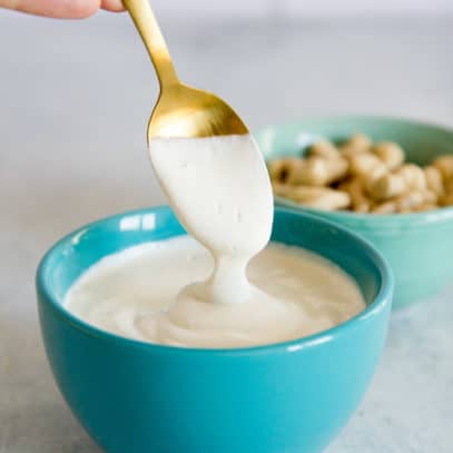 Spoon drizzling cashew cream into a turquoise bowl full of more cashew cream.