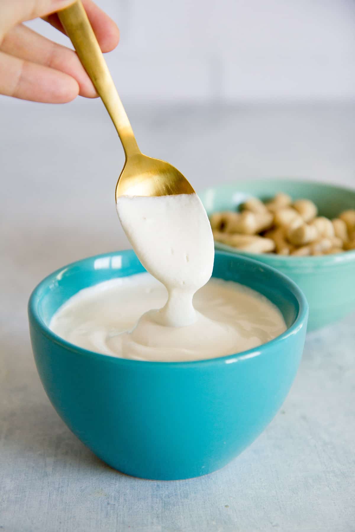 Spoon drizzling cashew cream into a turquoise bowl full of more cashew cream.