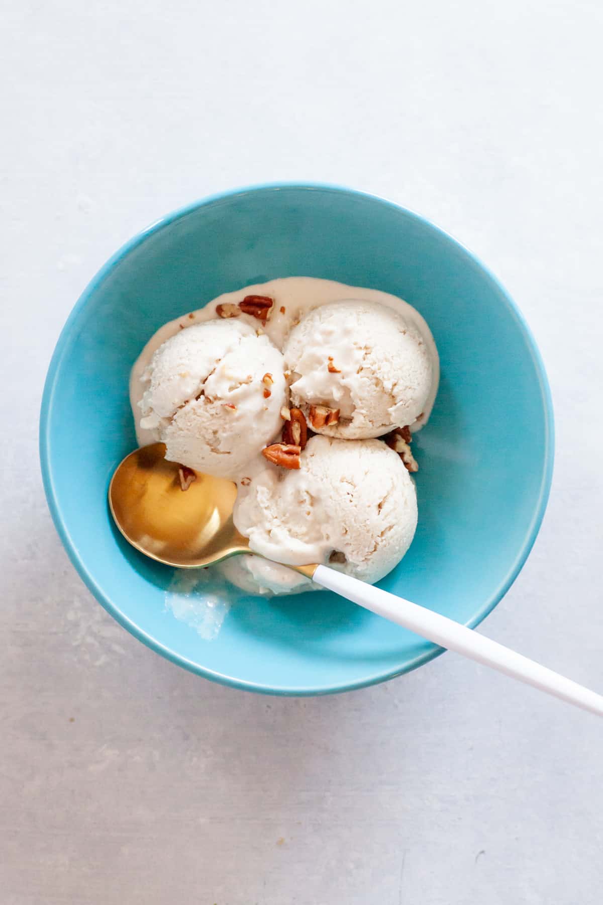 A gold spoon sits in a turquoise bowl with 3 scoops of cashew ice cream.